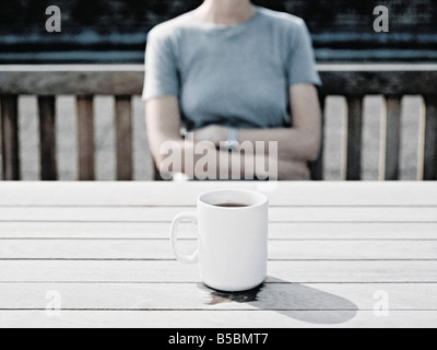 Junge Frau sitzt auf der Bank mit verschränkten Armen Stockfoto