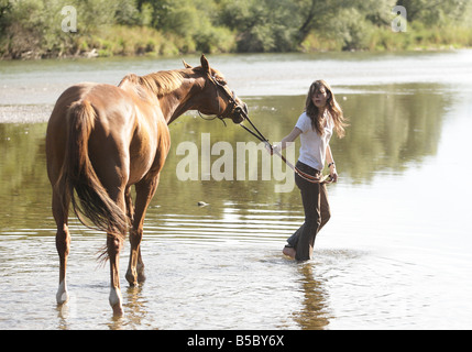 Teenager-Mädchen mit Pferd durch einen flachen Fluss zu Fuß. Stockfoto