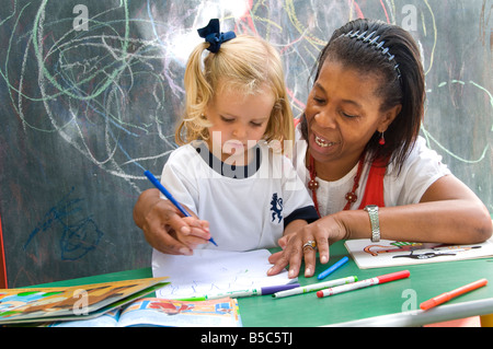 Kindergarten weiblich Lehrer Coaching blond 3-5 Jahre Kleinkind Mädchen zu Zeichnen Sie Formen draußen in sonnigen Schule Kindergarten Spielschule Stockfoto