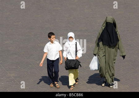 Eine Mutter mit zwei Kindern? im traditionellen Kleid zu Fuß durch die Djemaa El Fna - Hauptmarkt-Quadrat von Marrakesch. Stockfoto