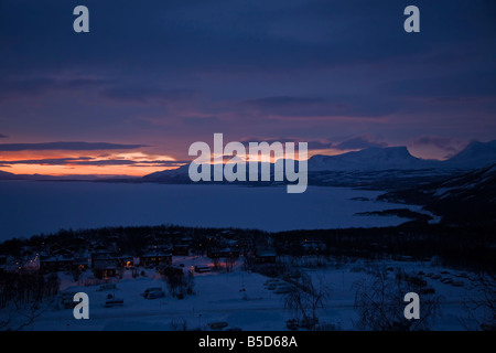 Die Sonne steht kurz vor dem Aufstieg über den vereisten See Tornetrask und das Dorf Bjorkliden in Lappland, Schweden Stockfoto