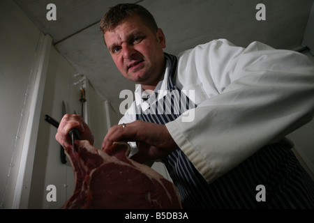 ein Portrait eines Metzgers, ein großes Stück Filetsteak mit einem großen scharfen Messer schnitzen. Stockfoto