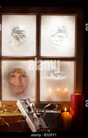 Österreich, Salzburger Land, junge Frau, die durch Fenster, Weihnachten Pakete und Kerzen im Vordergrund Stockfoto