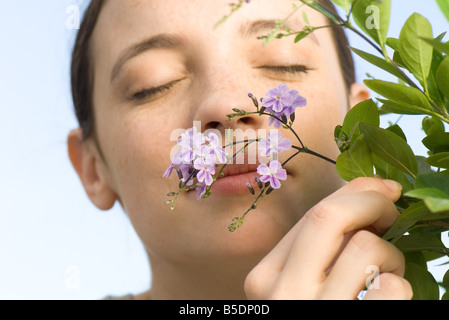 Junge Frau, die kleine lila Blüten auf blühenden Baum riechen Stockfoto