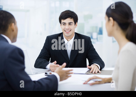 Geschäftsmann am Schreibtisch, im Gespräch mit Kunden und lächelnd Stockfoto