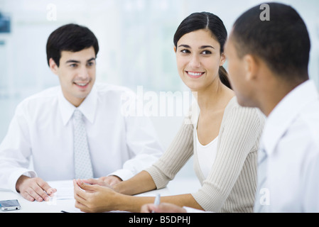 Junge Berufstätige sitzen am Tisch, konzentrieren sich auf Frau in Mitte Stockfoto