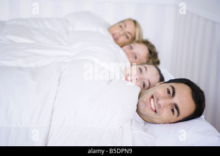 Familie liegen zusammen im Bett unter Tröster, lächelnd in die Kamera Stockfoto