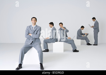 Geschäftsmann lächelnd in die Kamera mit Armen gefaltet, während seine Klone Laptops im Hintergrund verwenden Stockfoto