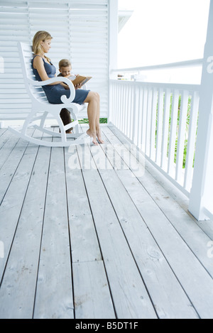 Frau sitzt im Schaukelstuhl auf der Veranda, Geschichte zu kleinen Jungen stehen an ihrer Seite zu lesen Stockfoto