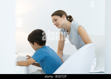 Junge, die Eingabe über Tastatur, Mutter über die Schulter schauen Stockfoto