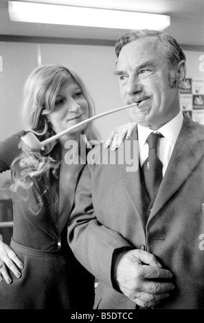 Pfeife rauchen-Champion Robert Locke von Hayes, Middlesex, verfolgt Schreibkraft Liliana Perez, wie der TV-Werbung während der britischen nationalen Pfeife rauchen Meisterschaft. ; Mai 1975 Stockfoto