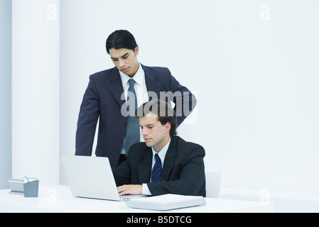 Geschäftsmann mit Laptop-Computer am Schreibtisch, Kollegen über die Schulter schauen Stockfoto