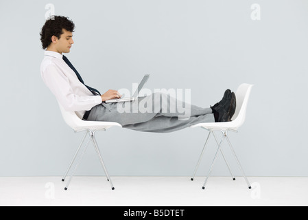 Geschäftsmann sitzt im Stuhl, die Füße auf einen anderen Stuhl, mit laptop Stockfoto