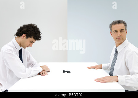 Geschäftsleute, die am Tisch, Schachfigur zwischen ihnen umgekippt Stockfoto