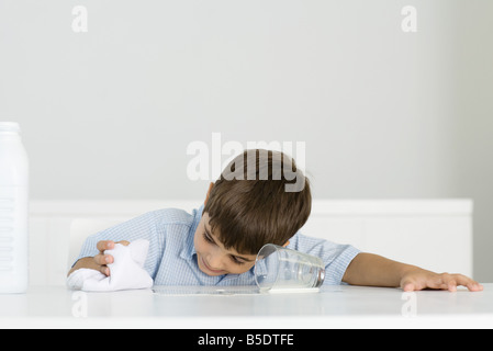 Jungen wischen Sie verschüttete Milch mit Handtuch Stockfoto