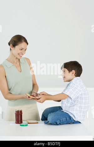 Mutter und Sohn bereitet Brot und Marmelade zusammen, Lächeln einander an Stockfoto