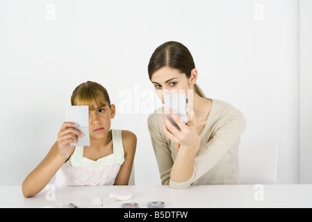 Mädchen und junge Frau sitzen nebeneinander, Blick in die Hand Spiegel, Kosmetik im Vordergrund Stockfoto