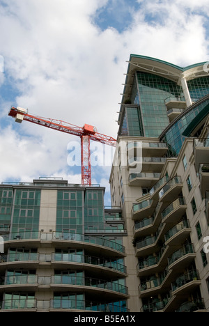 Ein Bild nach oben auf einem modernen Block aus London Wohnungen mit blauem Himmel ein Wolken. Ein große rote Kran ragt hinter. Stockfoto