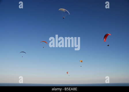 Sechs Gleitschirme fliegen friedlich hoch in den Himmel über dem Meer. Stockfoto