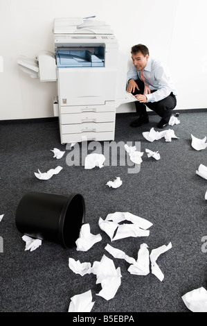 Geschäftsmann, hockend verzweifelt neben Kopiergerät Stockfoto