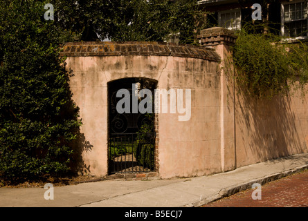 Ein schmiedeeisernes Tor führt in einem Garten hinter einer Mauer Ziegel und Stuck in Charleston, South Carolina. Stockfoto