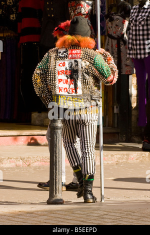 Camden Stables Markt Mann mit rot gefärbten Haaren holding Anzeige Brett in dotierten Jacke Gestreifte Hose schwarz Mütze & Stiefel Stockfoto