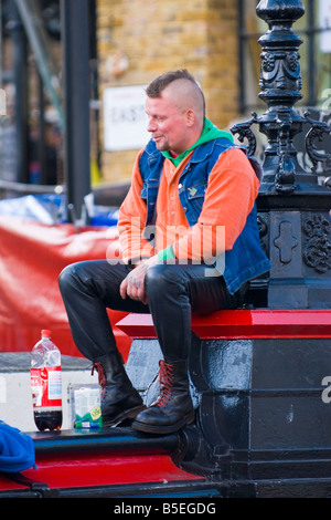 Camden Lock Market, sitzt Mann mit Irokesenschnitt braune Haare, Jeans und Stiefel Dr Martens auf Brücke über den Kanal im Gespräch mit Passanten Stockfoto