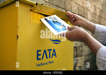 Man wirft eine Postkarte in einen gelben Briefkasten der Hellenic Post, Rhodos, Griechenland Stockfoto