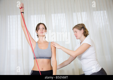 junge Frau, die Übungen mit Theraband sitzen auf Gymnastikball, beauftragt durch Physio-Therapeut Stockfoto