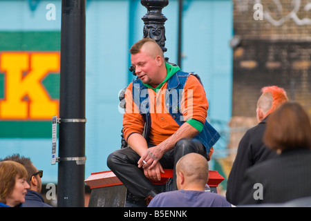 Camden Lock Market Mann mit Irokesenschnitt braune Haare, Jeans und Dr. Martens Stiefel sitzt auf Brücke über den Kanal im Gespräch mit Passanten Stockfoto