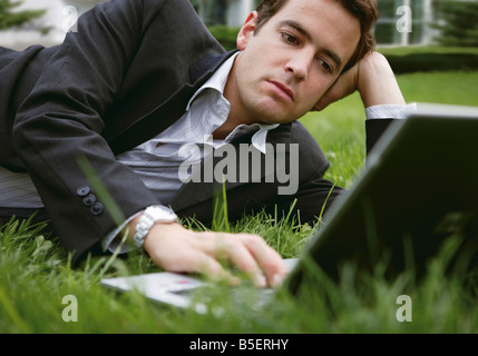 Geschäftsmann auf dem Rasen liegen, während mit einem laptop Stockfoto