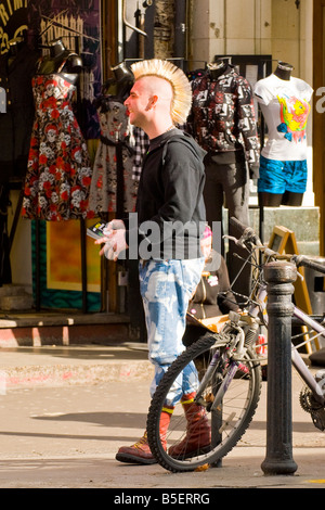 London, Camden Lock Market, lächelnden männliche junge mit Punk-Frisur blond gelb Hahnenkamm & Dr Martens Stiefel außen Kleidungsgeschäft Stockfoto