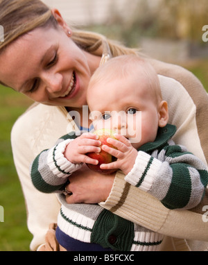 Eine junge Mutter lächelt halten Sie ihr Baby-jungen, der einen Apfel umklammert wird. Stockfoto