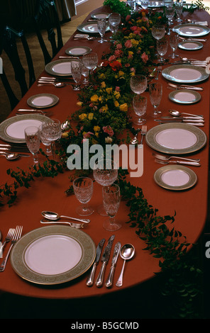 Frische Blumen und Silberbesteck und weißen Teller mit Goldrand eingestellt am langen Tisch mit rotem Tuch in traditionellen Speisesaal Stockfoto