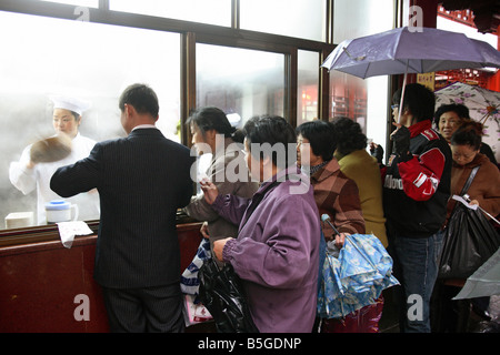 Fußgänger, die gerade eines Koch durch ein Fenster "Restaurant" Shanghai, China Stockfoto