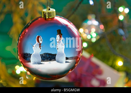 Zwei Schnee Männer und ein Feld der Schnee reflektiert in einem Weihnachtsbaum Ornament mit Zuckerstangen und Lichter Stockfoto