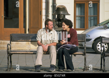 Junger Mann und Frau sitzen auf Bank mit Statue von Napoleon am Hlavne Namestie (Hauptplatz) in Bratislava, Slowakei Stockfoto