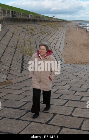 Ältere Dame, die zu Fuß am Strand von Aberdeen im Wind Scotland UK Stockfoto