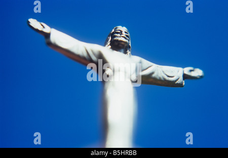 Impressionistische Jesus Christus-Figur in Silber mit ausgestreckten Armen Ansicht von unten mit klaren blauen Himmel dahinter Stockfoto