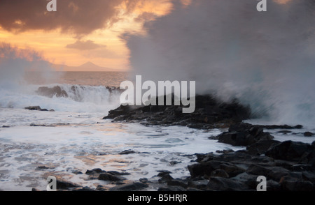 Wellen, die auf Felsen bei Sonnenuntergang. El Confital, Las Palmas, Gran Canaria. Galdar in der Ferne Stockfoto