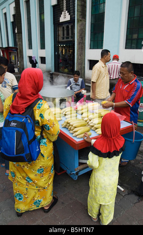 Eine Frau und Kind das Tragen der roten Kopftuch um einige heiße maiskolben von einem Straßenhändler in Kuala Lumpur, Malaysia Stockfoto