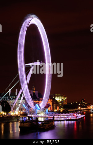 London Eye Ferris Wheel London United Kingdom | LONDON, United Kingdom — Eine lange Exposition verschwimmt das sich drehende London Eye in einen soliden Ring aus Licht über der Themse, hinter dem sich die Silhouette der County Hall befindet. Das von Marks Barfield Architects entworfene und 2000 eröffnete 135 Meter (443 Fuß) auskragende Rad dreht sich mit etwa 0,26 m/s und ist so langsam, dass seine Bewegung auf der Kamera zu einem durchgehenden Band wird. Es bleibt das höchste auskragende Beobachtungsrad der Welt. Stockfoto