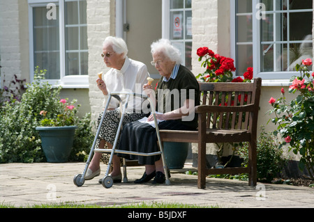2 ältere Frauen sitzen saß zusammen essen Eiscreme-Kegel-Leute sitzen auf einer Bank Stockfoto
