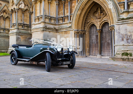 Ein renovierter, flaschengrüner Lagonda-Oldtimer aus den 1930er Jahren, der mit weißen Hochzeitsbändern vor der Wells Cathedral in Somerset, England dekoriert ist. Stockfoto