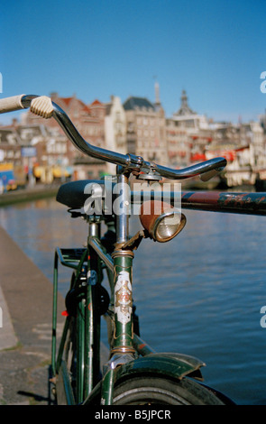 Altes grün gefärbtes rostiges Fahrrad, das neben Geländer und Kanal in Amsterdam an hellem sonnigen Herbsttag geparkt ist. Stockfoto