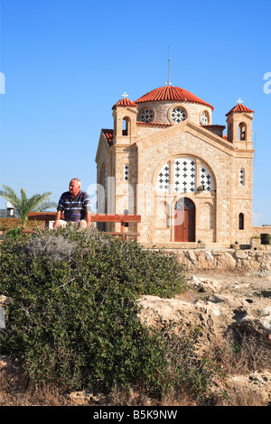 Mann sitzt auf der Bank vor Agios Georgios Tis Pegeias Kirche an der Westküste Zyperns Stockfoto