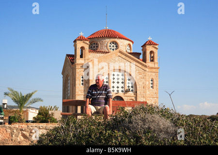 Mann sitzt auf der Bank vor Agios Georgios Tis Pegeias Kirche an der Westküste Zyperns Stockfoto