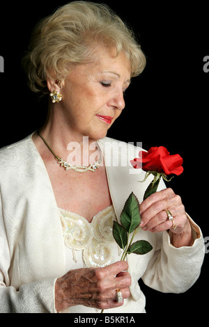 Eine schöne ältere Dame hält eine Rose trägt sie ein Hörgerät Stockfoto