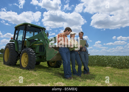 Zwei Männer und eine Frau mit Blick auf einen Laptop und stützte sich auf einen Traktor Stockfoto