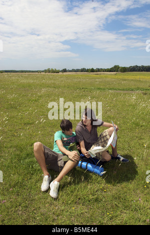 Zwei männliche Rucksacktouristen sitzen auf einer Weide und Blick auf eine Karte Stockfoto